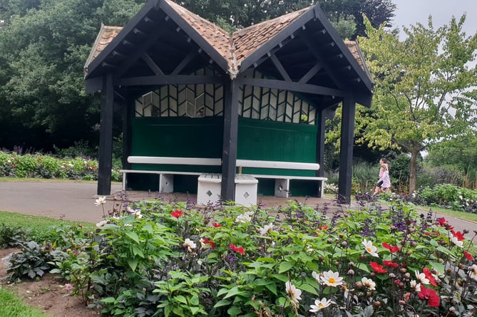 A view of the 'thrupenny' shelter surrounded by flower beds in Wellington Park.